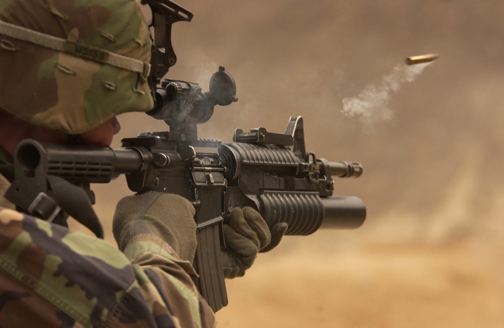 Soldier firing a rifle, spent casing in mid-air